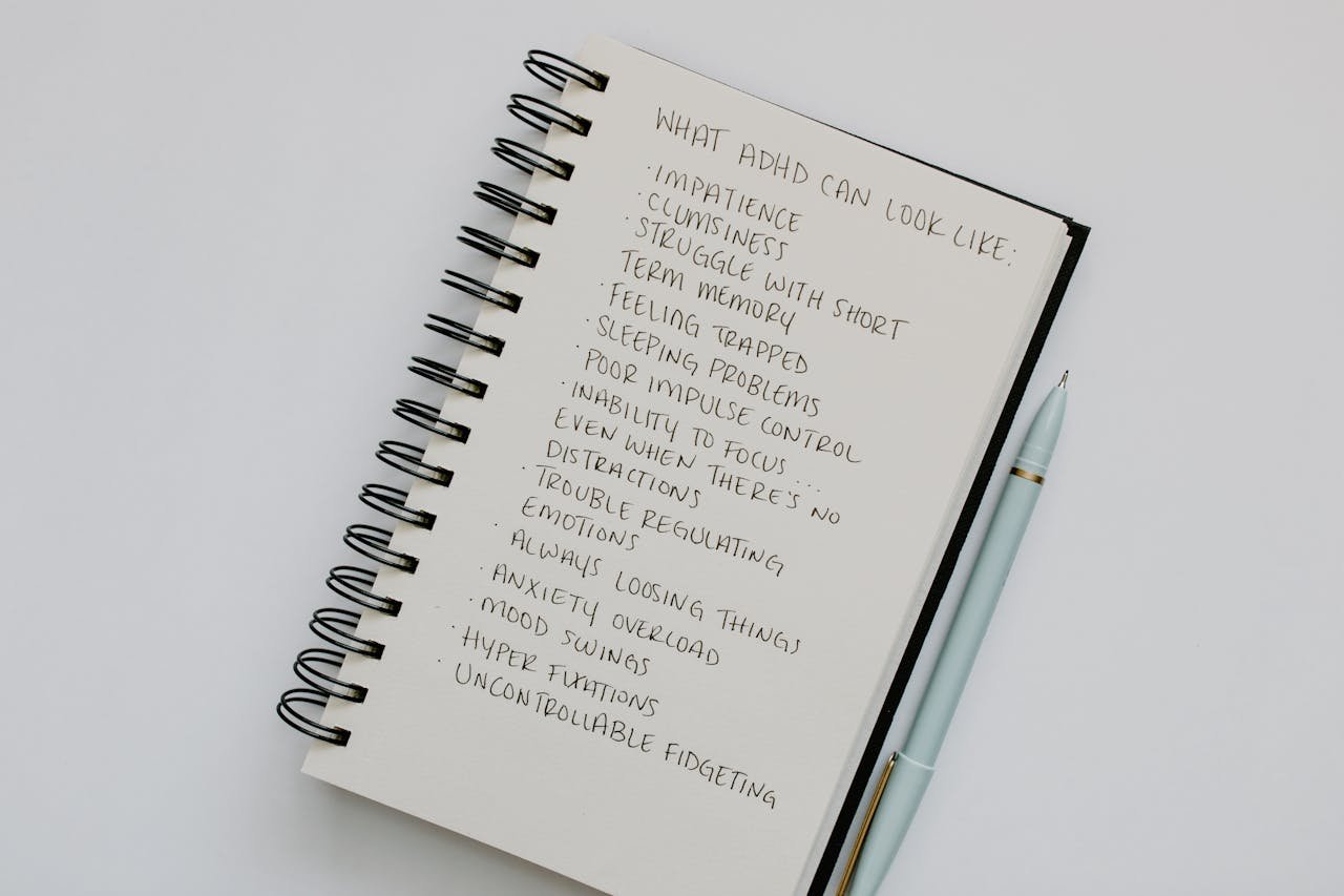 Notebook open with handwritten list of ADHD symptoms, featuring a pen alongside.